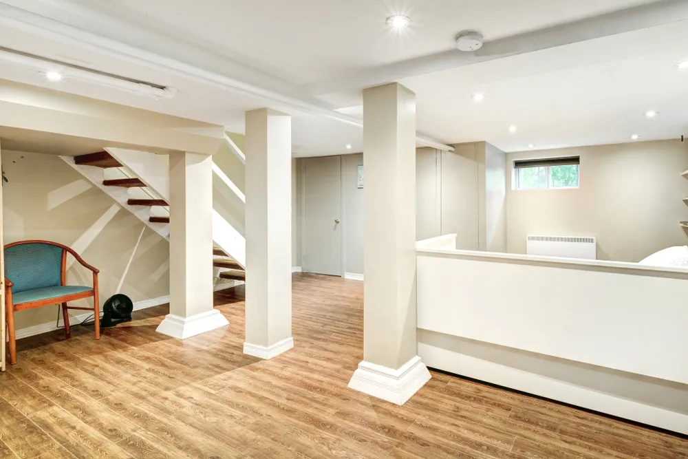 Finished basement with medium brown wood-look LVP flooring, support columns, and recessed lighting.