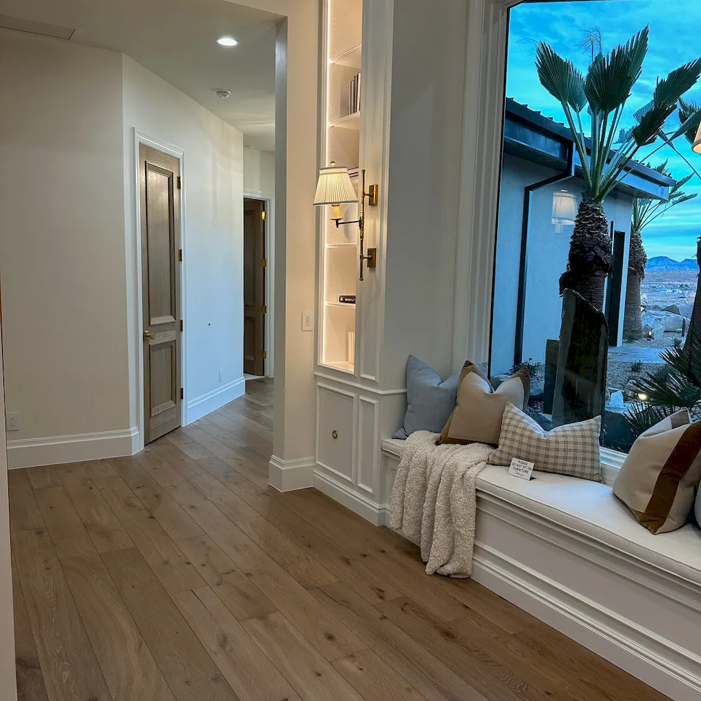 Light-toned wide-plank hardwood in a hallway with a cushioned window seat and Southern Utah desert view through large windows.