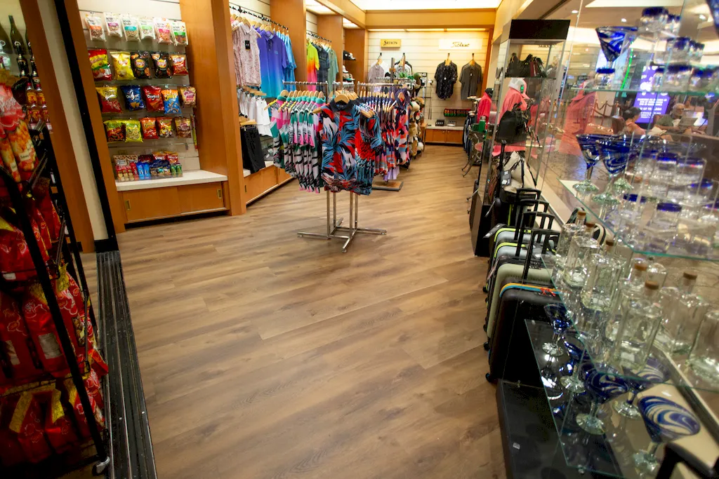 Wide view of medium-brown wood-look commercial flooring in a retail gift shop with clothing and snack displays.